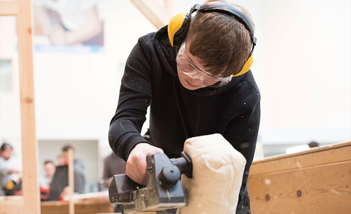 Image of a young male wearing ear defenders whilst doing carpentry work.