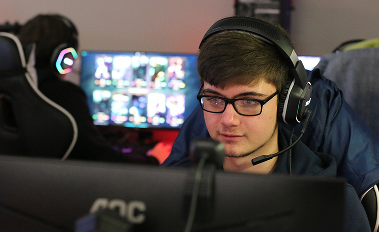 Image of a young male esports player wearing a gaming headset and looking down towards a computer monitor.