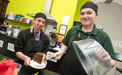 Image of two young learners serving cake.
