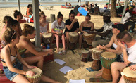 Image of a group of young people playing drums on a beach
