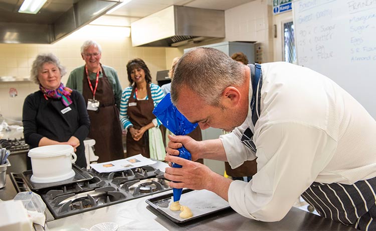 Photo of a group of adults watching a chef pipe icing on to a baking tray