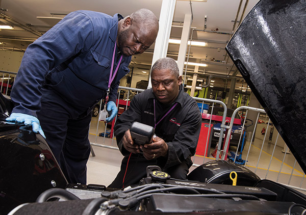 Image of two men in overalls working on a car engine.