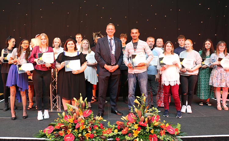 Group photo of a college principal stood in front of a large group of students holding certificates and awards.